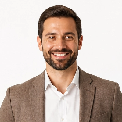 Retrato de um homem a sorrir, de cabelo escuro e barba, com blazer castanho e camisa branca.
