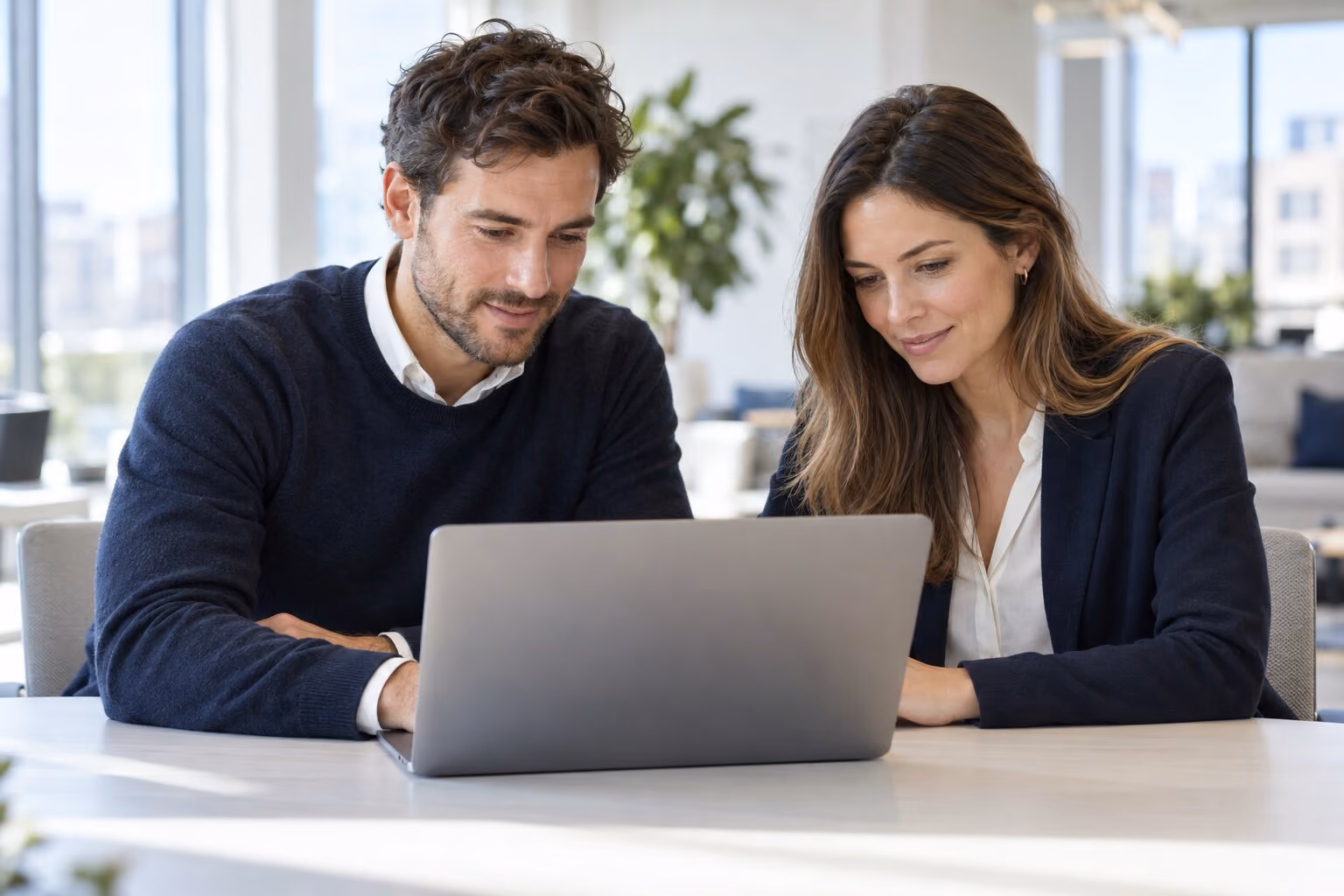 Dos personas del equipo revisando juntas una laptop en una oficina moderna.