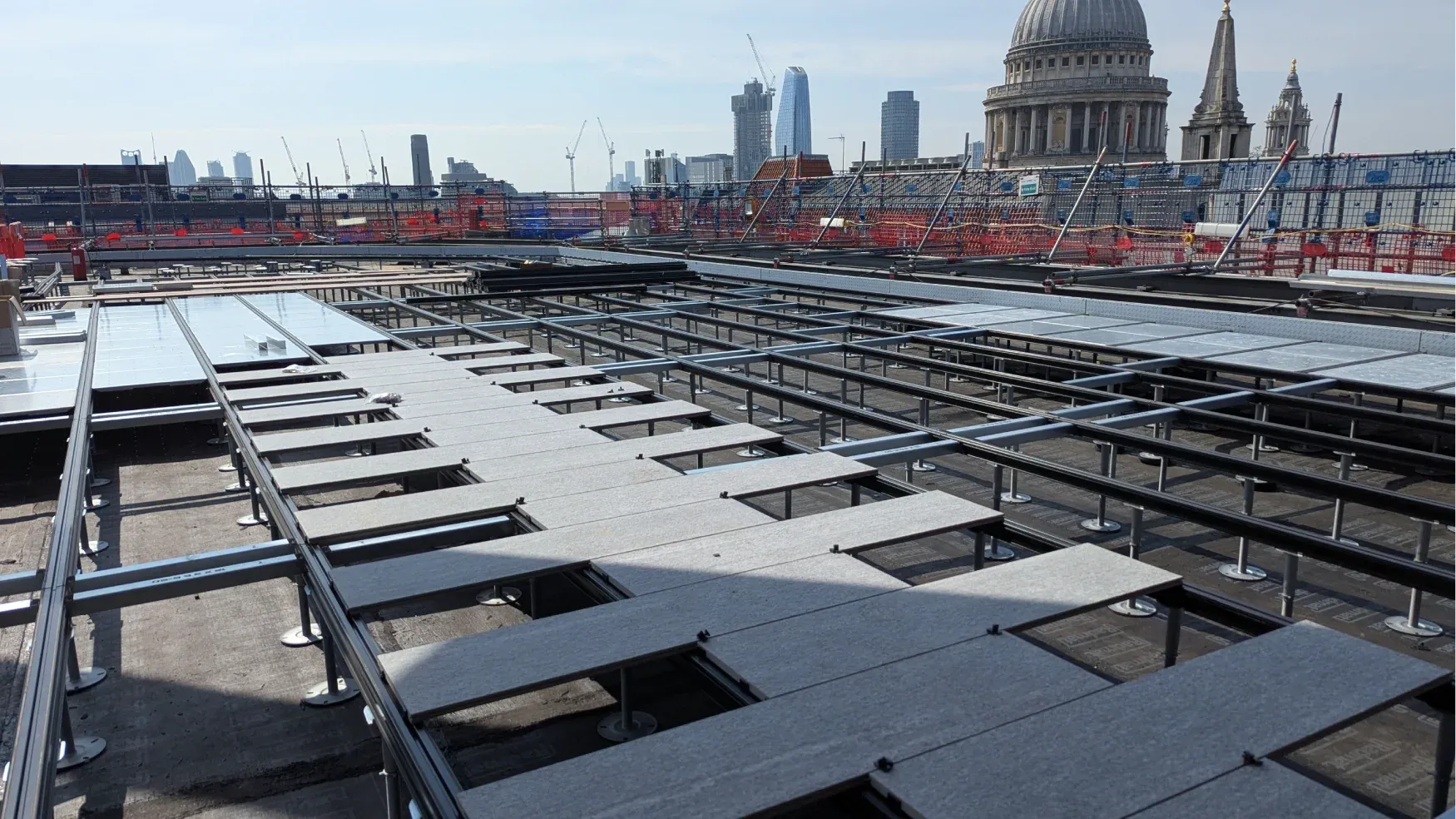 Metal framework being installed on rooftop with city skyline and domed building in background.