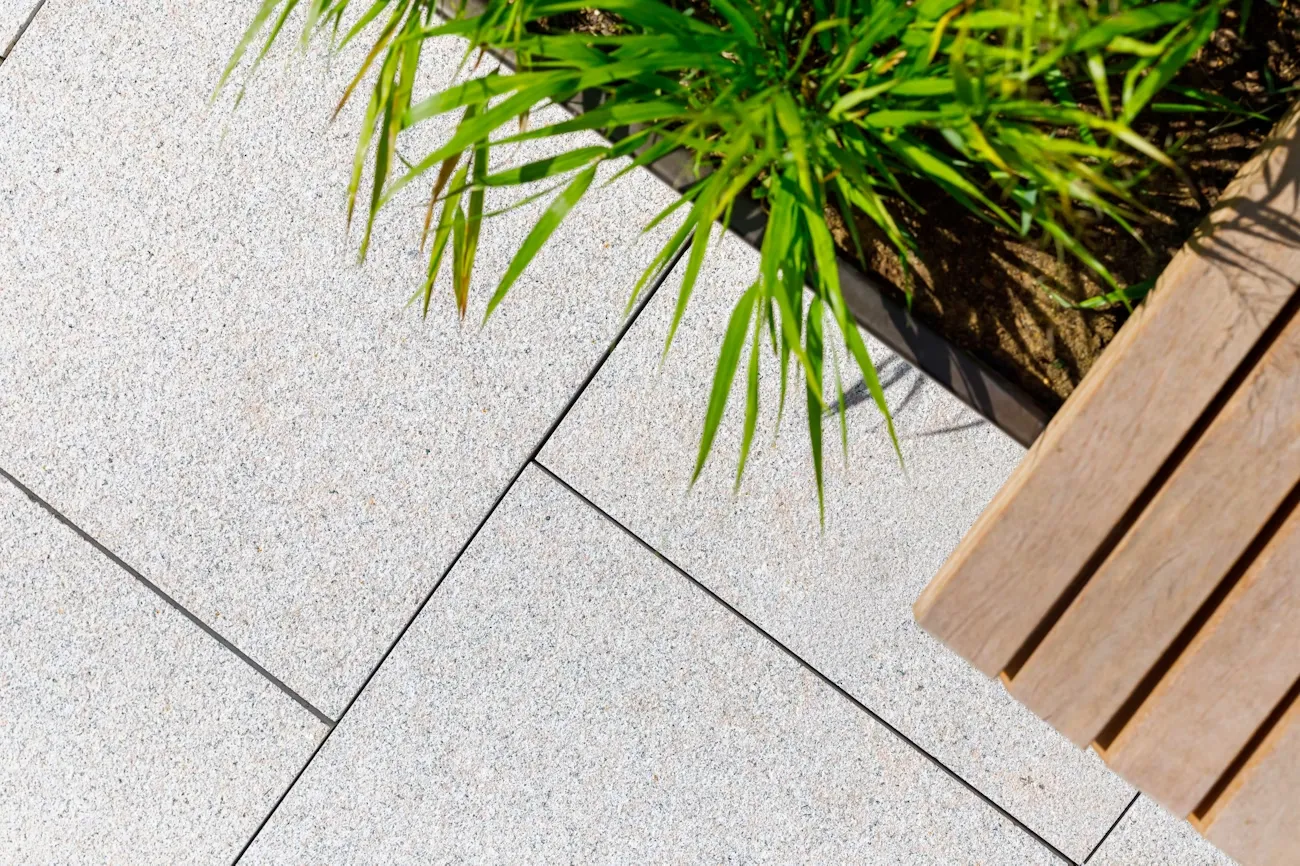 Light gray stone tiles beside green plants and a wooden bench.
