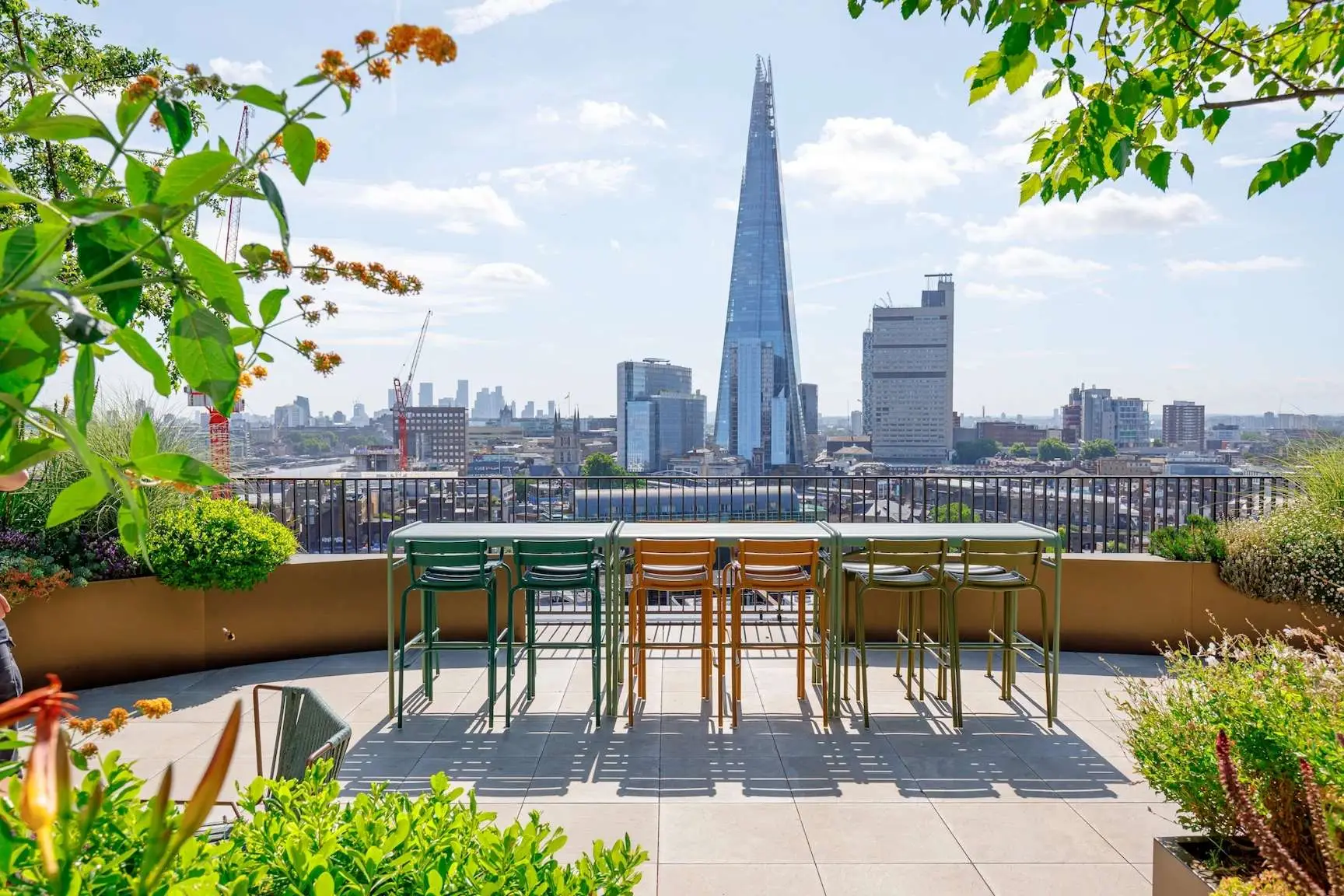 Outdoor terrace with high tables and chairs overlooking London skyline with the Shard on a sunny day.