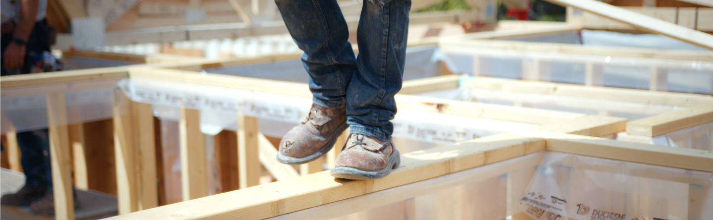 Close-up of worker's worn boots standing on wooden framing at a construction site.