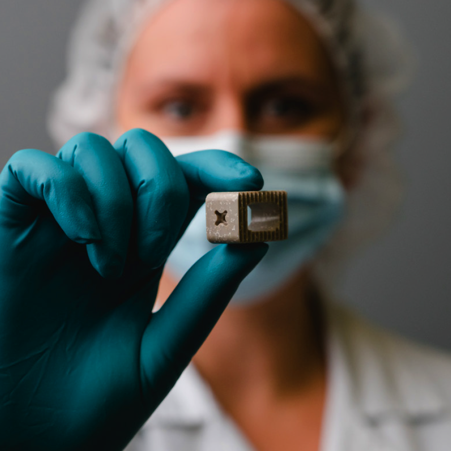 Scientist in mask and gloves holding an Octane Exo spinal implant up to the camera.