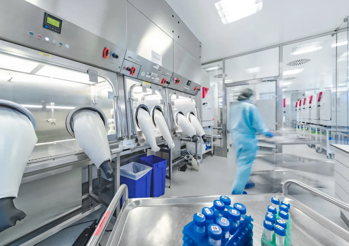 Cleanroom with isolator workstations and glove ports; an operator walks past a cart of sample vials.