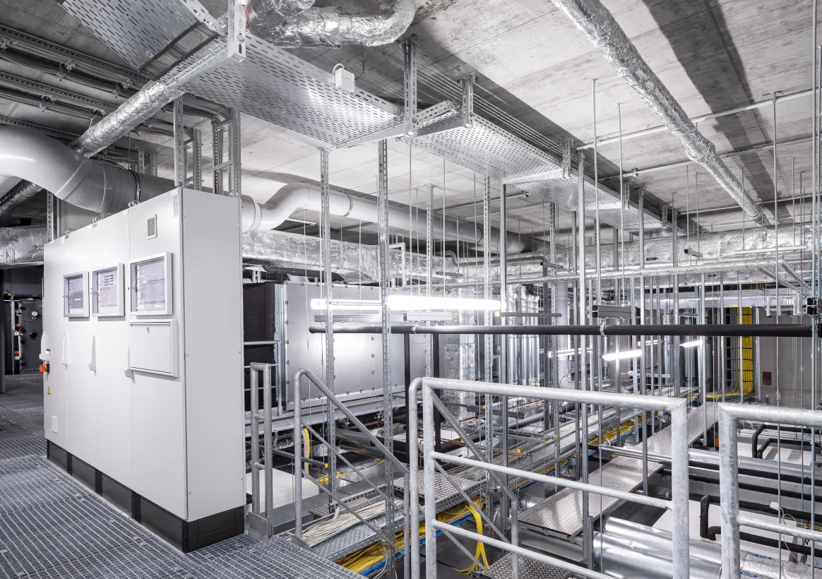 Plant room with ventilation ducts, metal walkways and control cabinets.