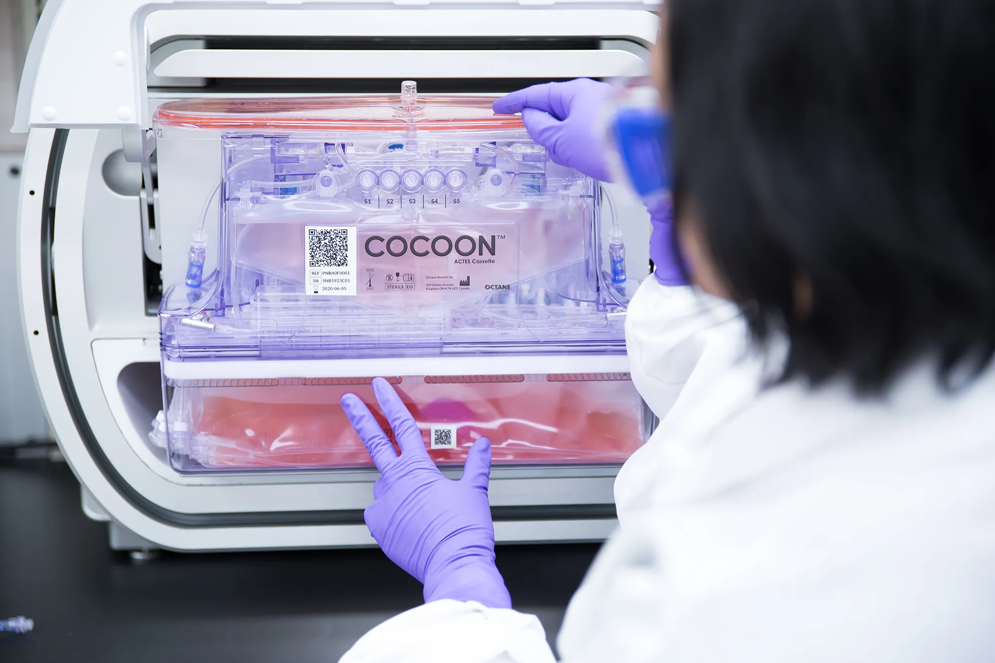 Operator in purple gloves loading a cassette into a Cocoon Platform instrument.