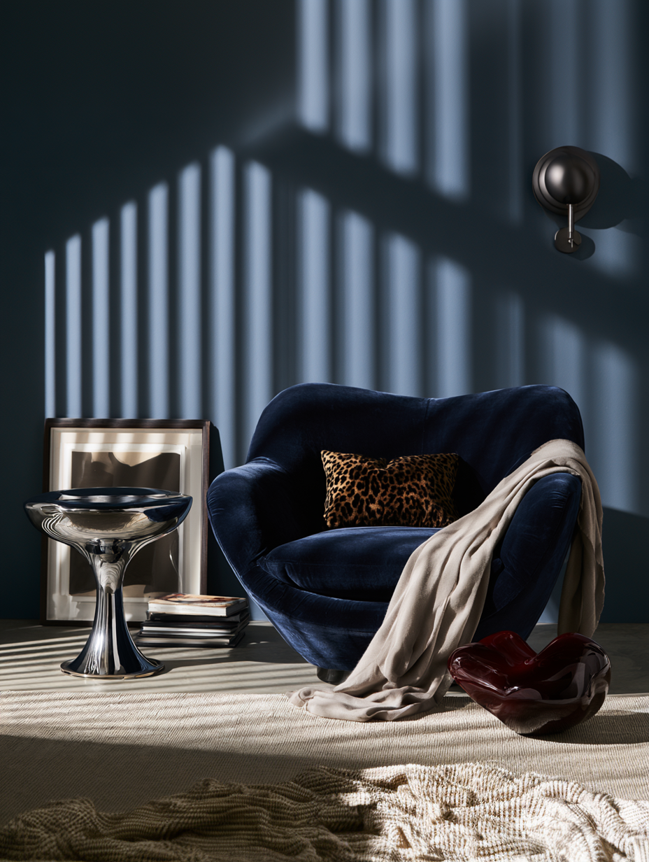 Blue velvet armchair with leopard pillow and beige throw, next to silver side table and dark heart sculpture.