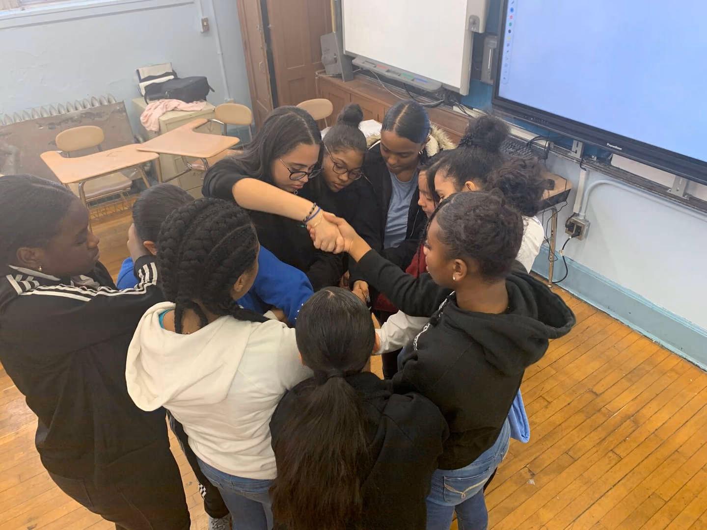 Students joining hands together in a classroom team huddle