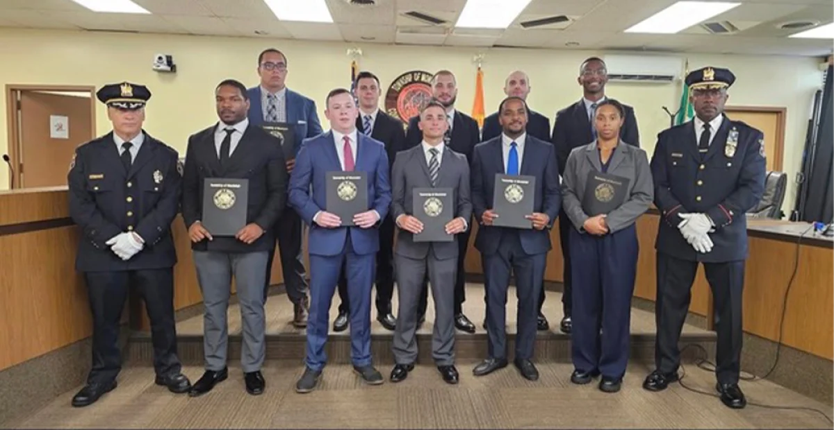 Group of people in formal attire holding certificates, flanked by two police officers in uniform.