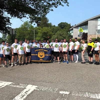 Group of people in white shirts holding a New Jersey State PBA banner outdoors on a sunny day.