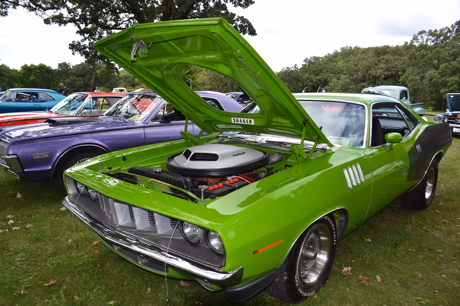 Green muscle car with hood open on display at a car show