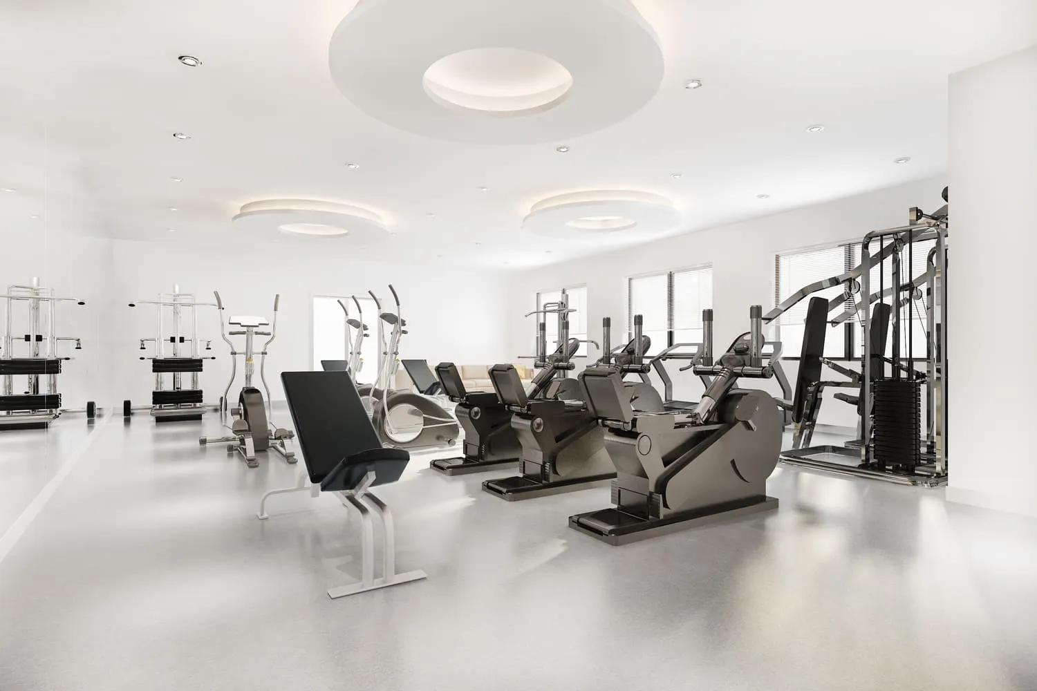 Modern spacious gym with various exercise machines including stationary bikes, elliptical trainers, weight machines, and a bench, illuminated by circular ceiling lights.