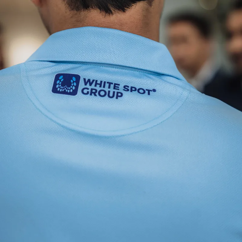Back of a person wearing a light blue shirt with the White Spot Group logo printed near the collar.