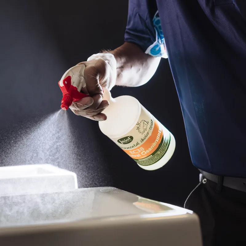 Person wearing gloves spraying disinfectant cleaner from a spray bottle onto a surface.