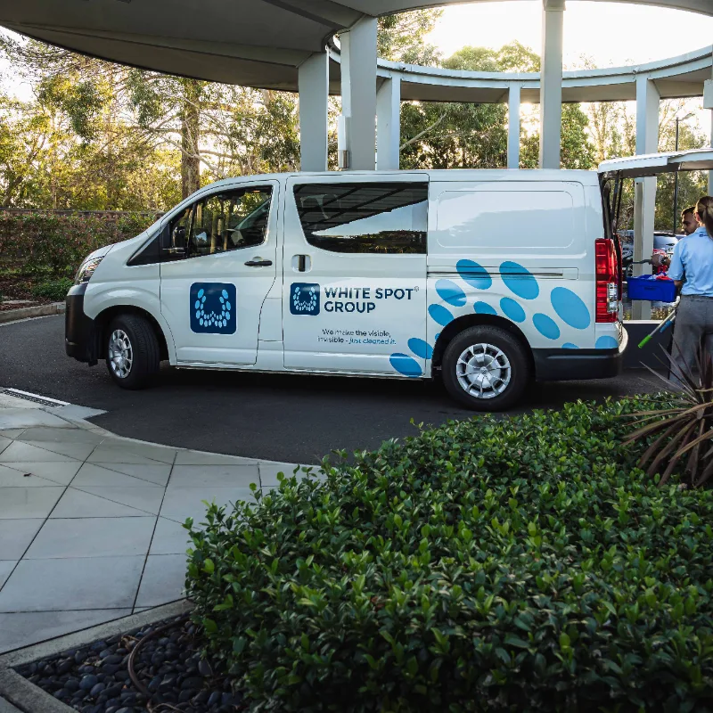 White delivery van with White Spot Group logo parked near greenery under a curved roof structure.