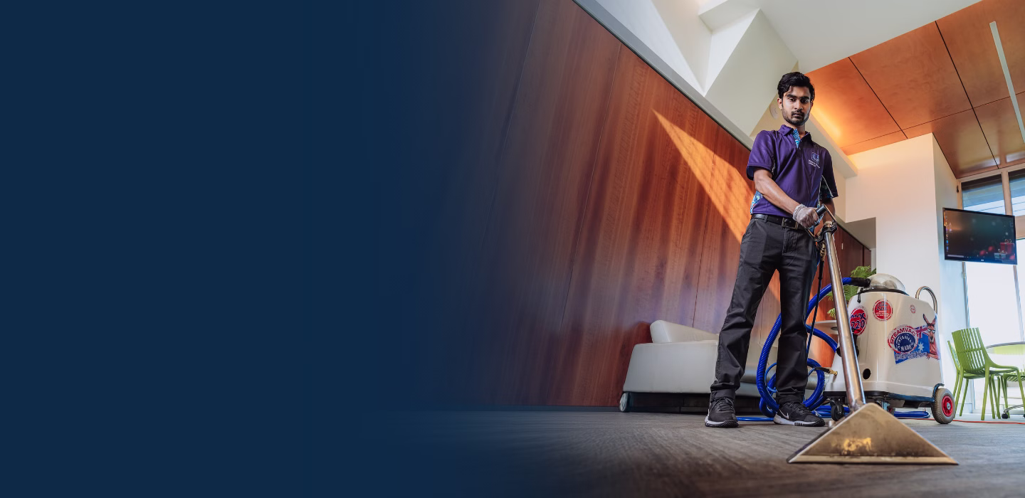 Man using professional carpet cleaning equipment in a modern office space with wooden wall panels and green chairs.