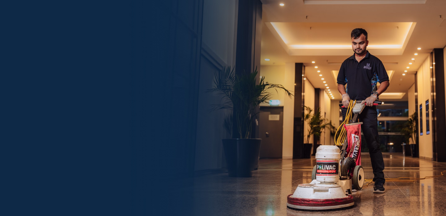 Man operating a floor polishing machine in a well-lit modern corridor with potted plants.