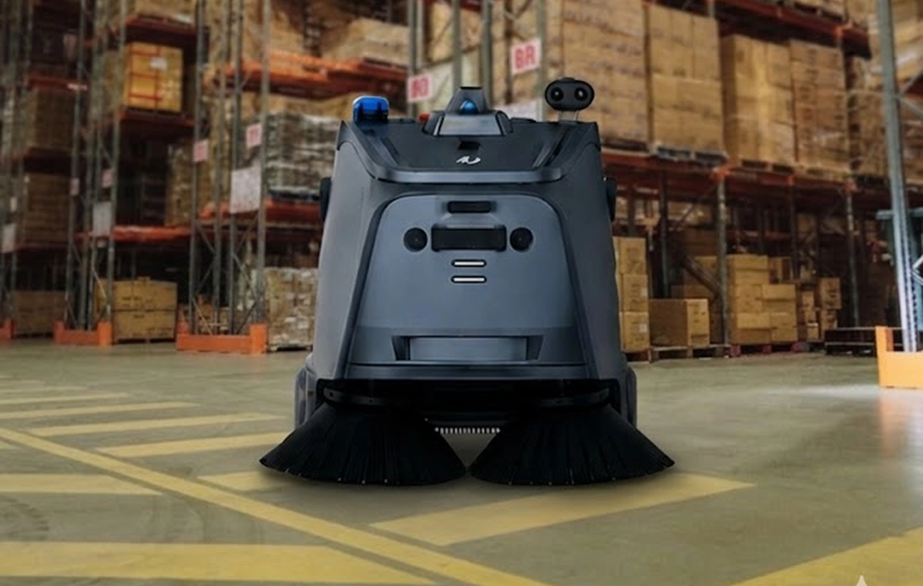 Autonomous warehouse floor cleaning robot with rotating brushes in an industrial storage area.