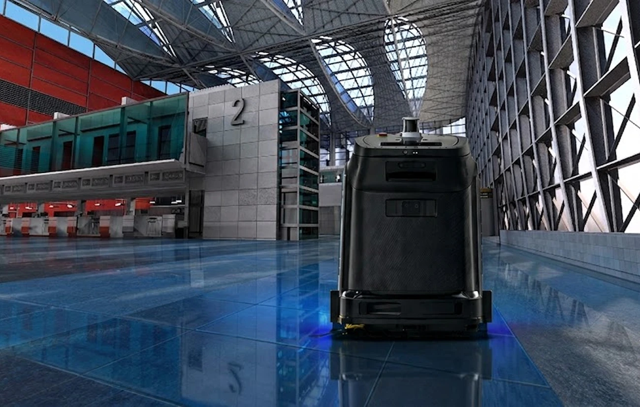 Automated floor cleaning robot operating in a spacious modern indoor terminal area.
