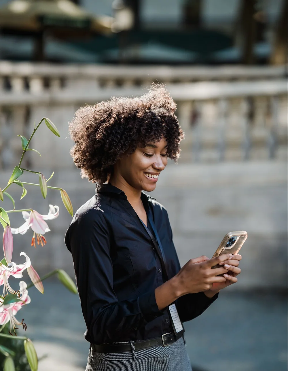 Une jeune femme sourit en lisant un message sur son smartphone, dans la rue