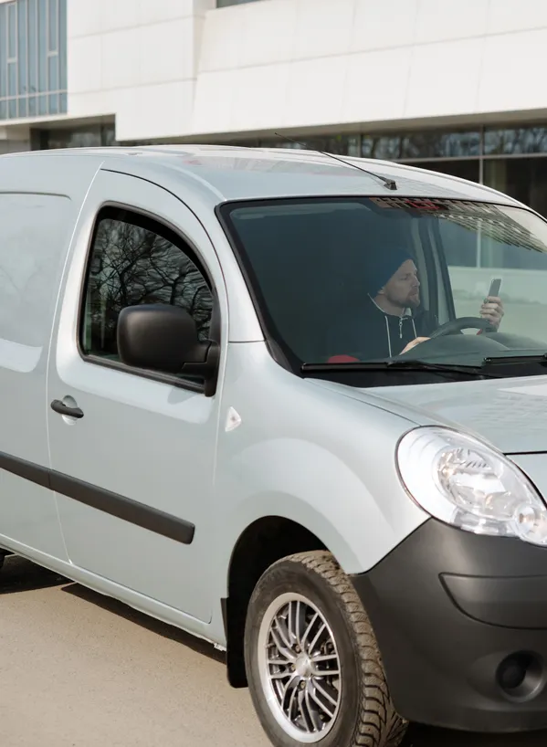 Un artisan lit un message sur son téléphone au volant de sa camionnette utilitaire