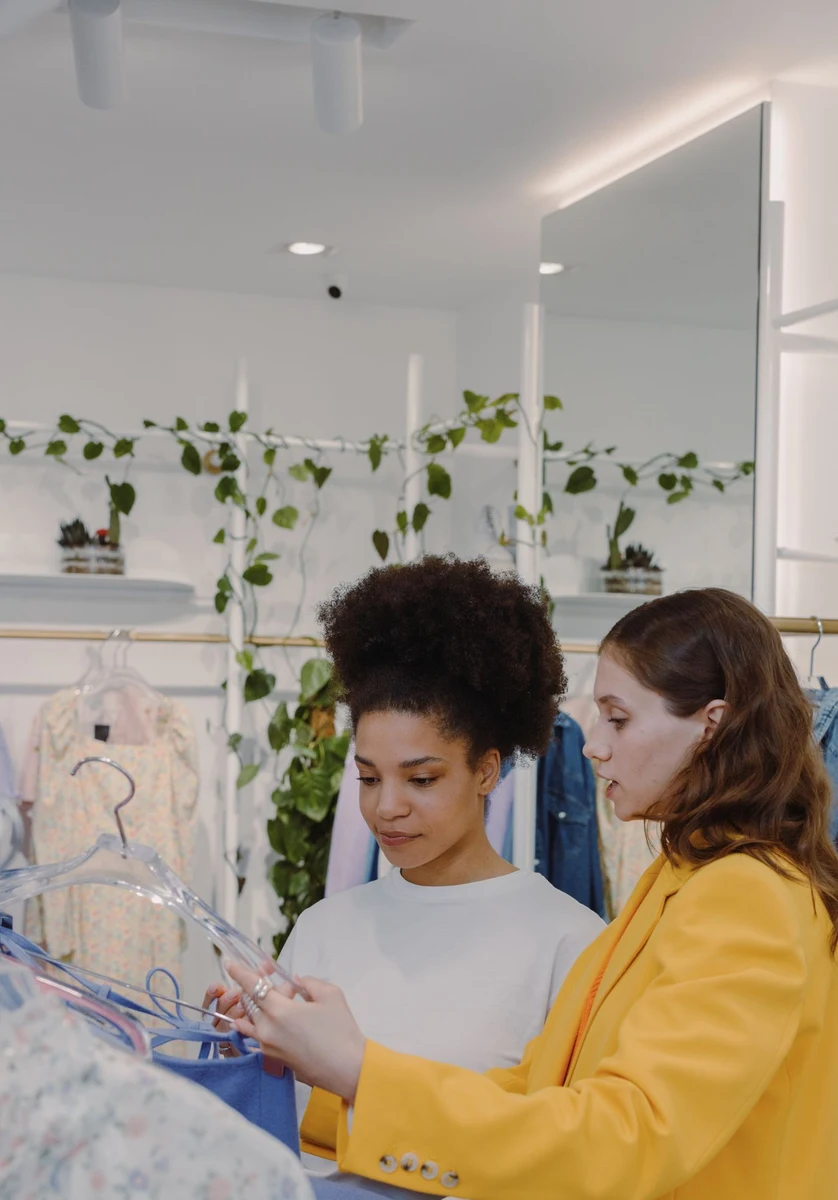 Une vendeuse conseille une cliente devant un portant, dans une boutique lumineuse