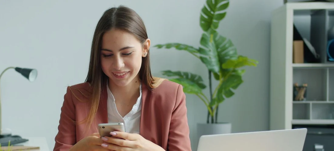 Une conseillère sourit en répondant à un message sur son téléphone, à son bureau