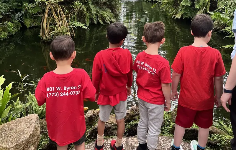 Black Bear Academy students in red school shirts look out over a pond at a botanical conservatory