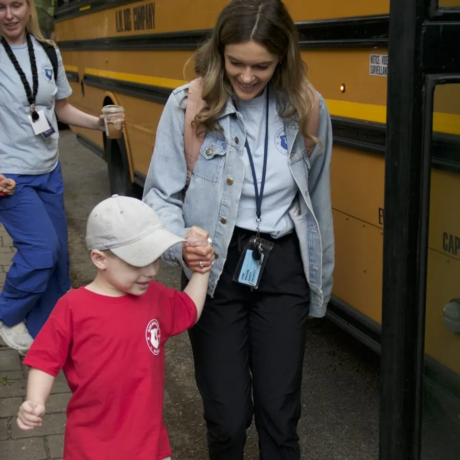 A Black Bear Academy teacher holds a child's hand as they step off the school bus