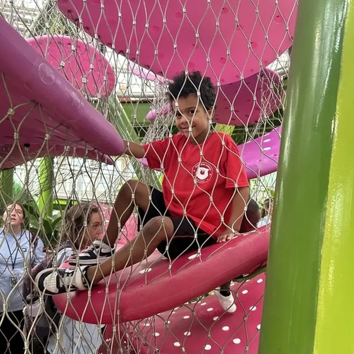 A child in a Black Bear Academy shirt smiles from a climbing net