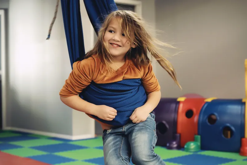 A child smiles in a hanging sensory swing at Black Bear Academy