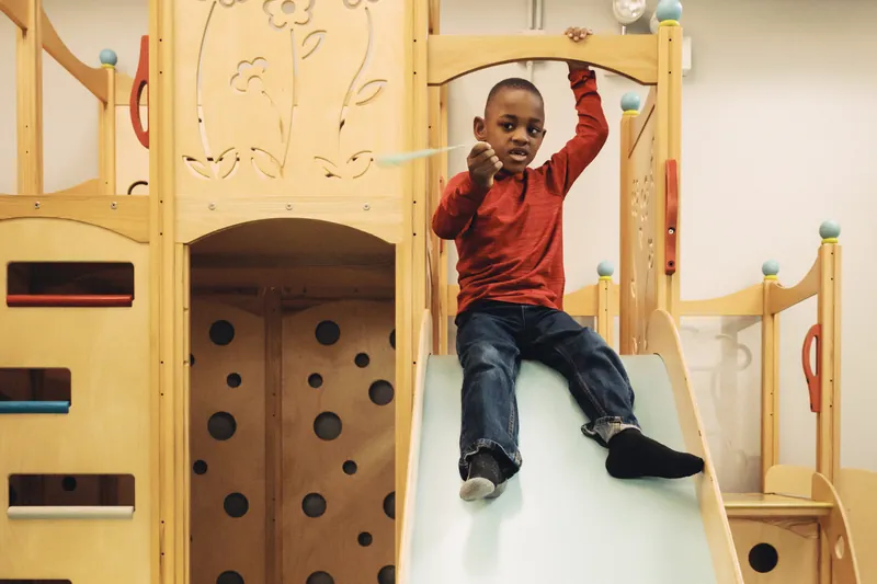 A child comes down the slide of the climbing structure in Black Bear Academy's indoor gym