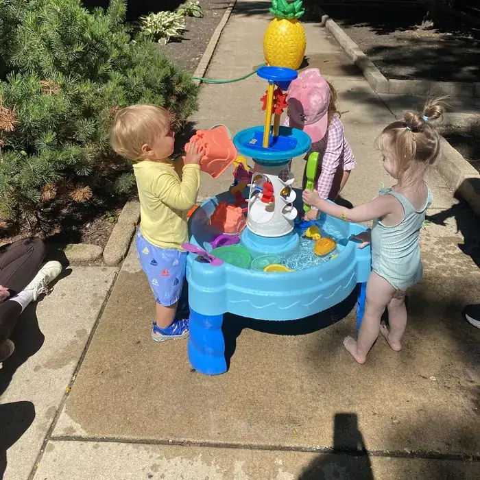 Toddlers splash at a water table outside the school on a sunny day