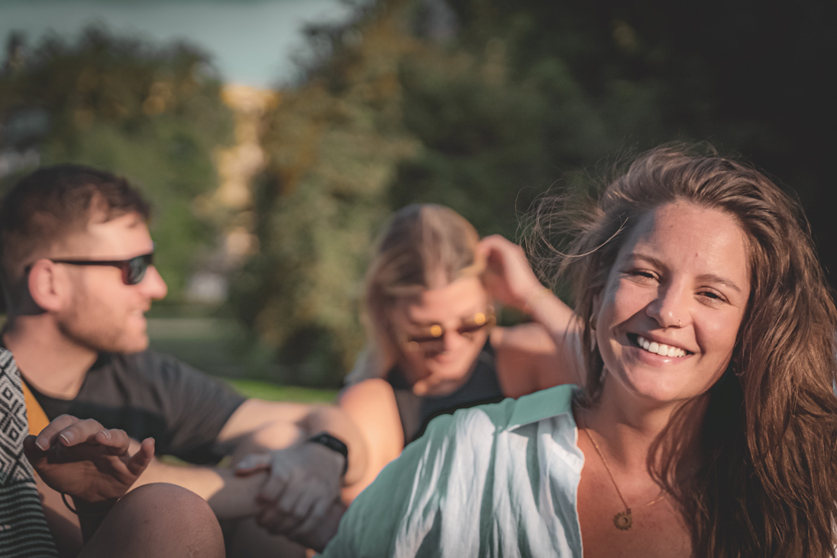 Alina Zimmermann lächelt im Freien in die Kamera, hinter ihr steht eine Gruppe von Menschen in der Sonne.