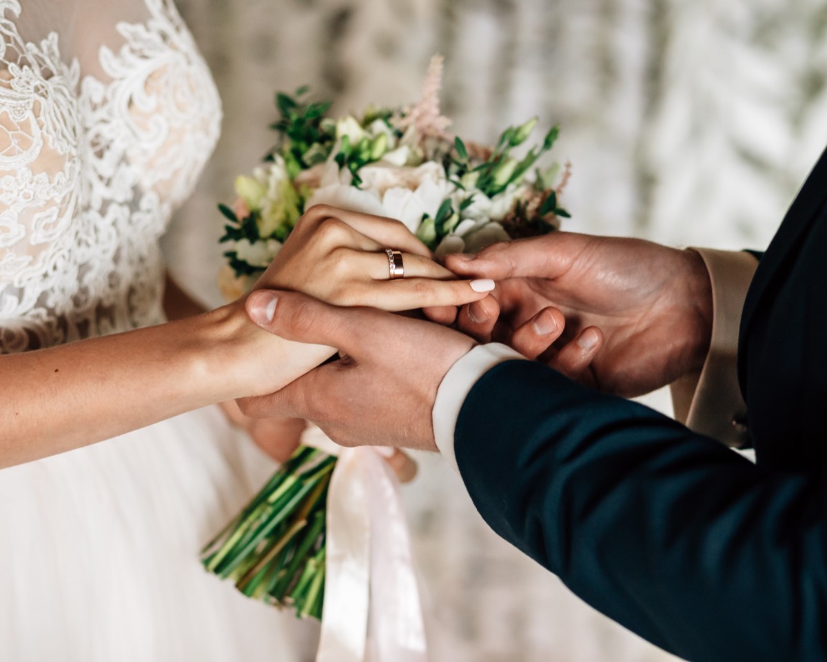 Bride and groom exchange rings holding bouquet during wedding ceremony