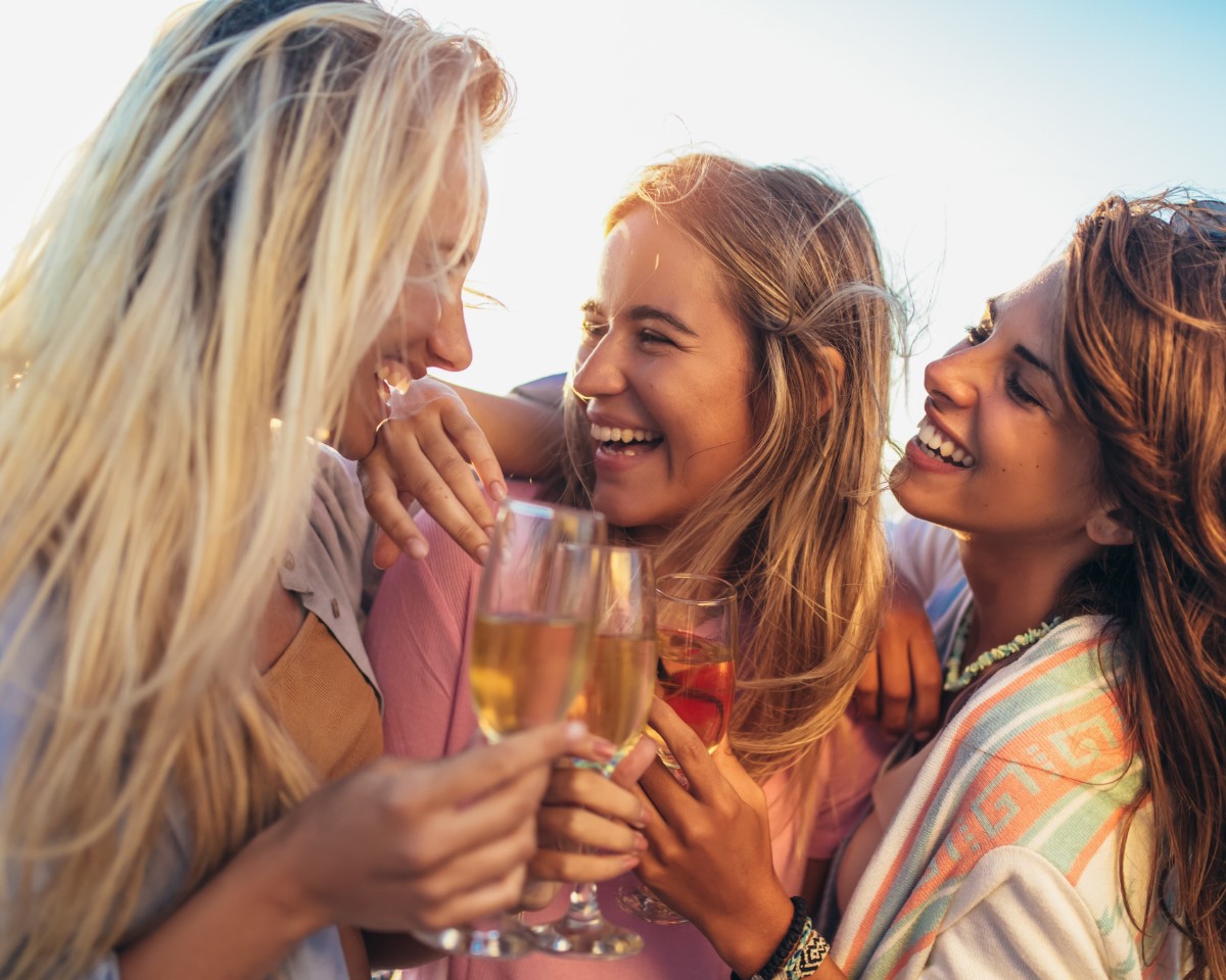 Group of three friends laughing and celebrating with drinks on a sunny getaways vacation