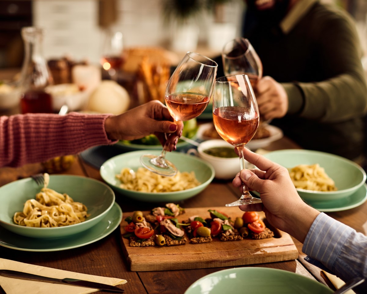 People clinking wine glasses at indoor dining table.