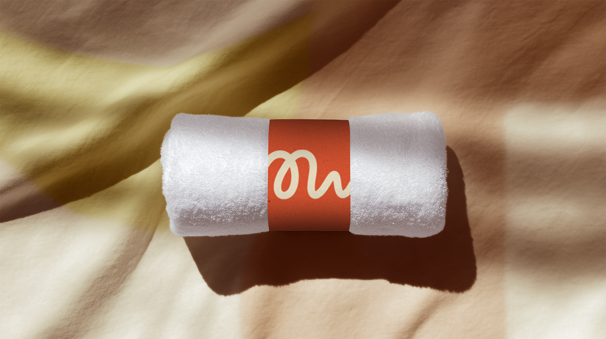 Rolled Muscle Health white towel wrapped with an orange band on a crumpled beige and yellow fabric surface.