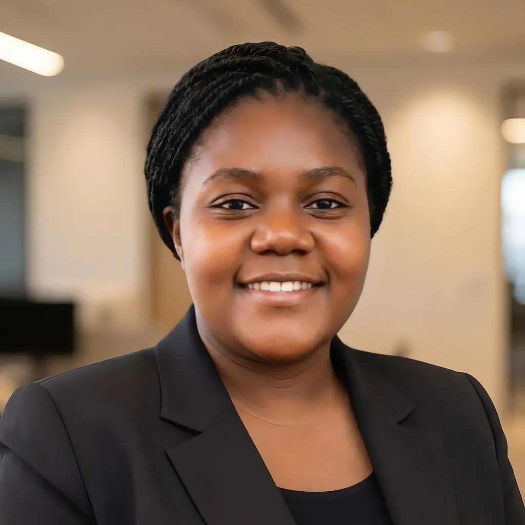 Portrait of a smiling woman with braided hair wearing a black blazer and top in an office setting.