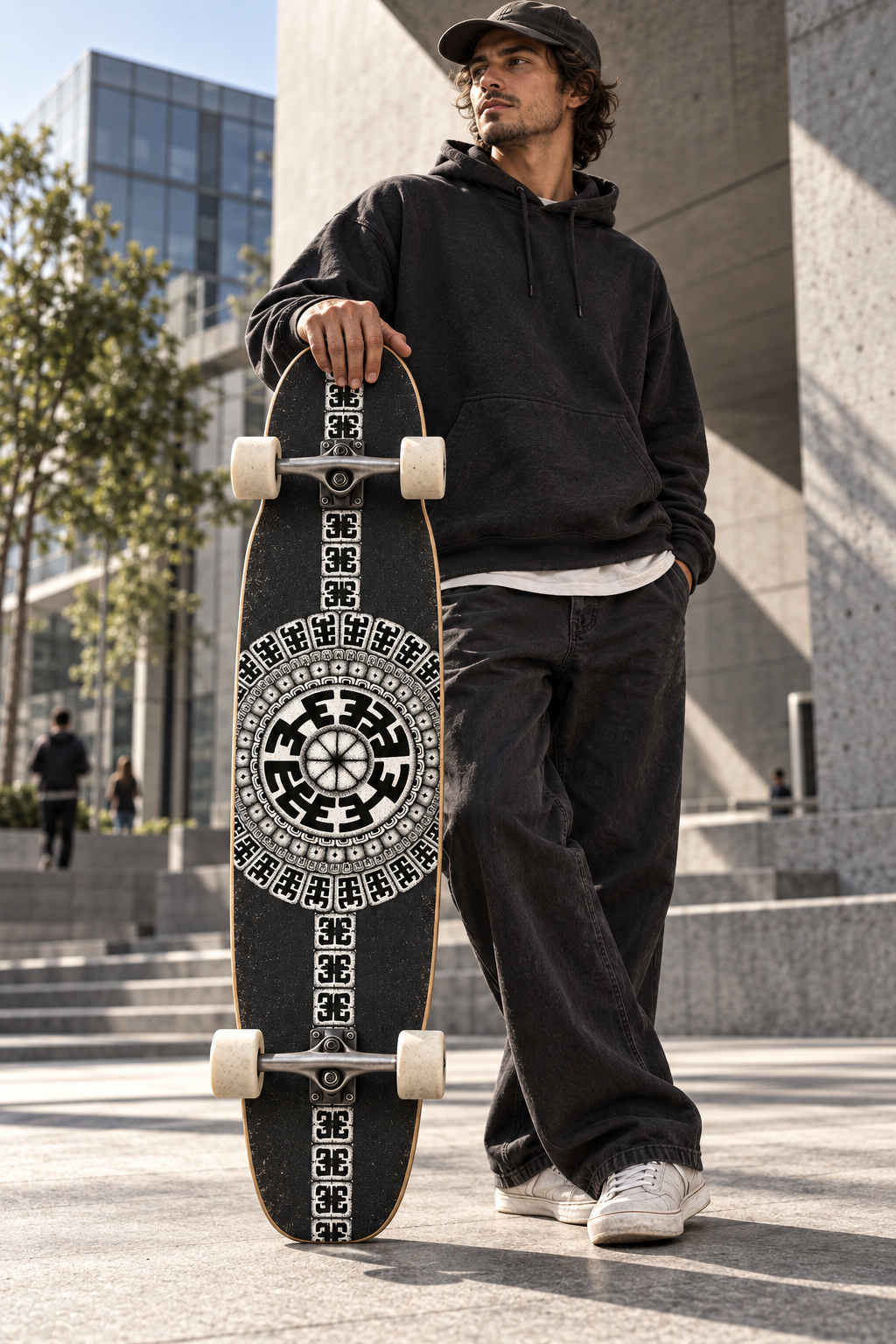 Skateboarder holding a black longboard with the Komo mandala and geometric border in an urban plaza.