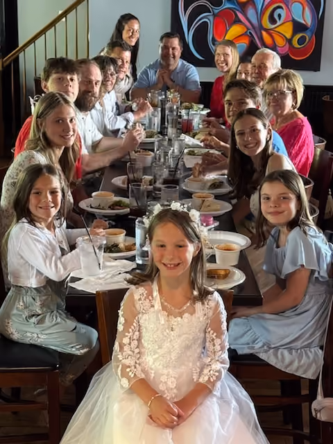 Family of adults and children gathered around a long table enjoying a meal together indoors.