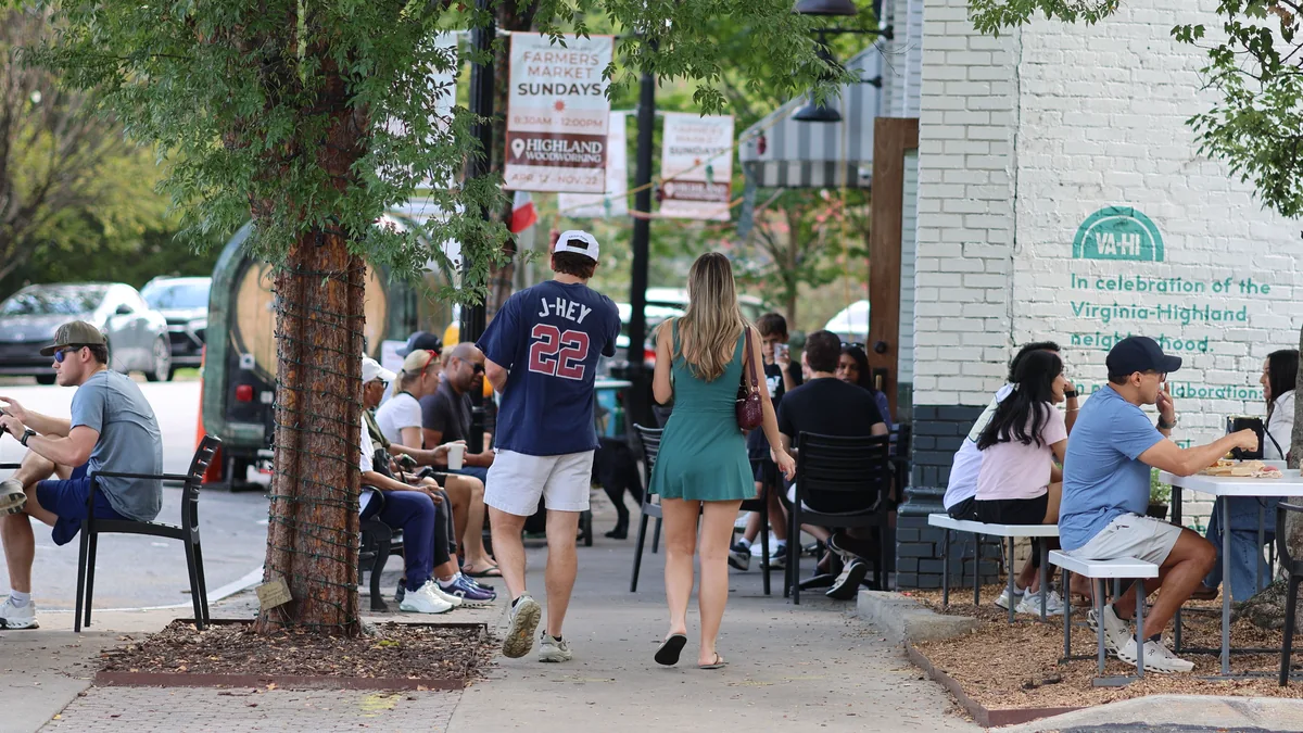 Pedestrians on the sidewalk near shops with a Farmers Market Sundays banner