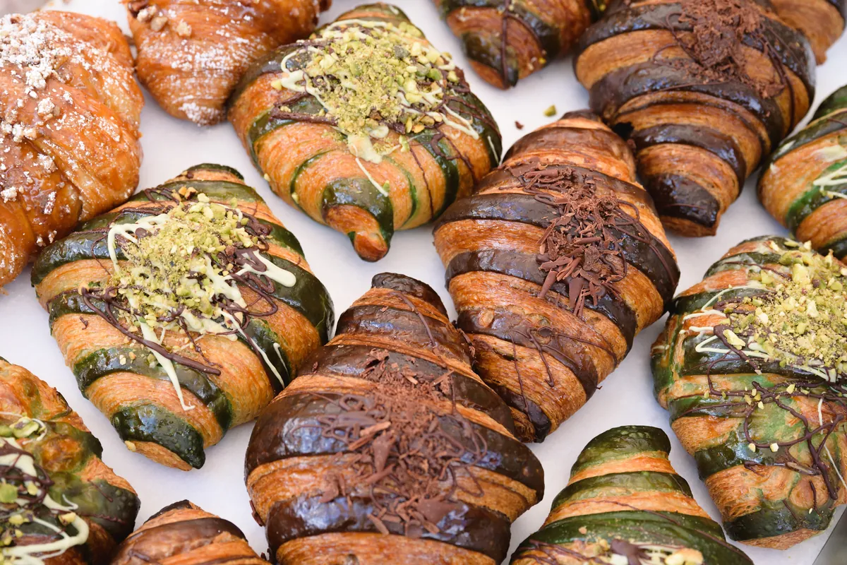 Close-up of chocolate and pistachio-topped pastries arranged at a farmers market bakery stall.