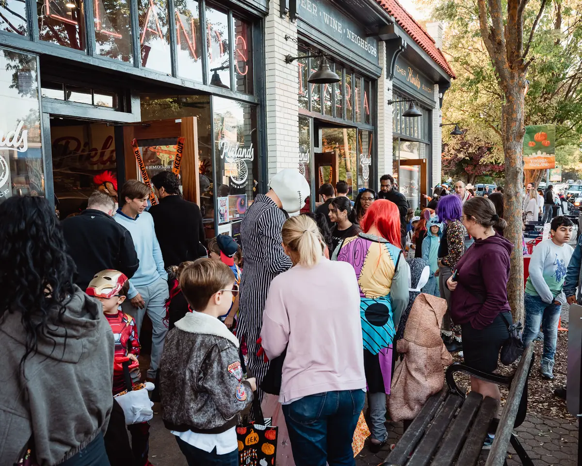 A crowd of children and families in Halloween costumes gathered outside a storefront during Candy Crawl.