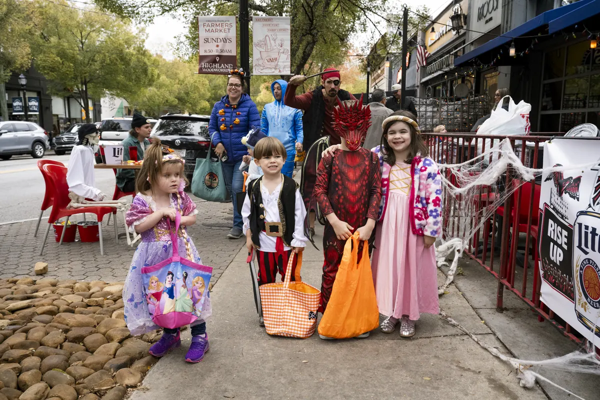 A group of children in Halloween costumes, including a princess and a dragon, pose on a decorated street during Candy Crawl.