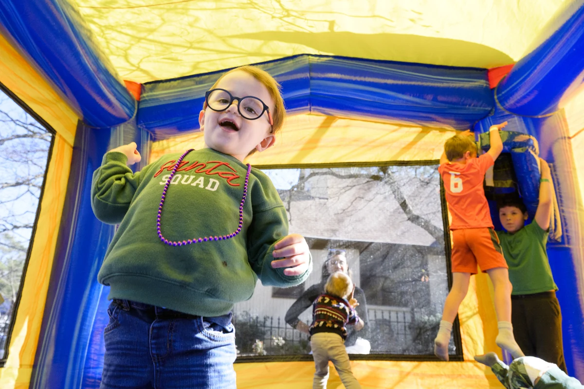 A child laughing inside an inflatable bounce house, with other kids playing behind him.