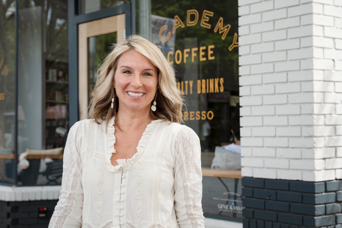 Lindsay Wheeler, President and Co-Founder of Virginia Highland District, smiling in front of a coffee shop storefront