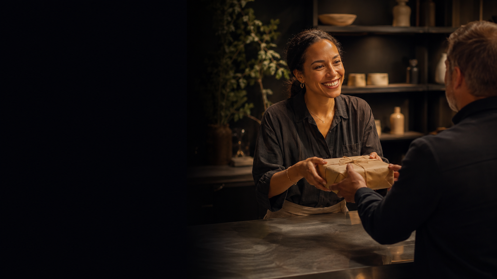 A shop owner handing a wrapped paper parcel across the counter to a returning customer at dusk