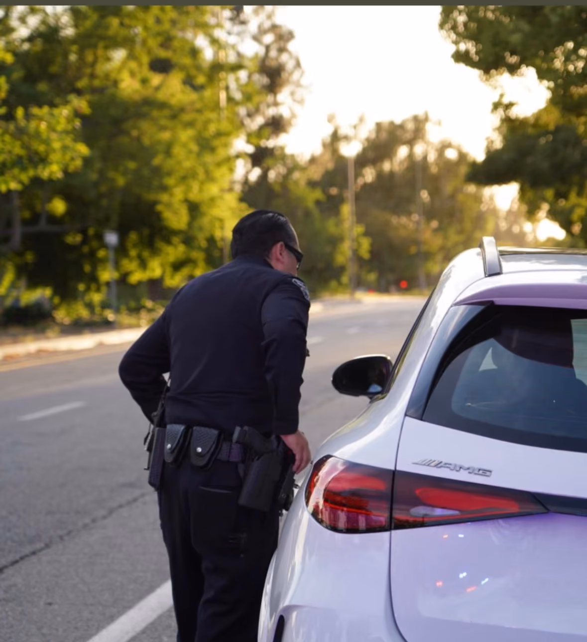 Sierra Madre Police officer standing beside a patrol vehicle on a tree-lined street