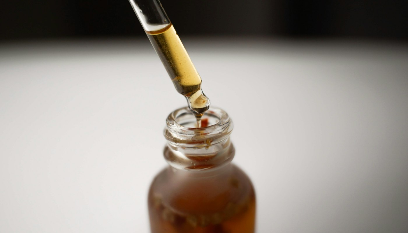 A dropper of concentrated liquid herbal extract above an amber glass bottle